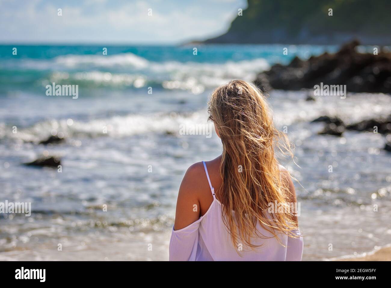 A young beautiful girl looks at the sea, the wind develops her blond hair.  White dress, blue water., beautiful view Stock Photo - Alamy