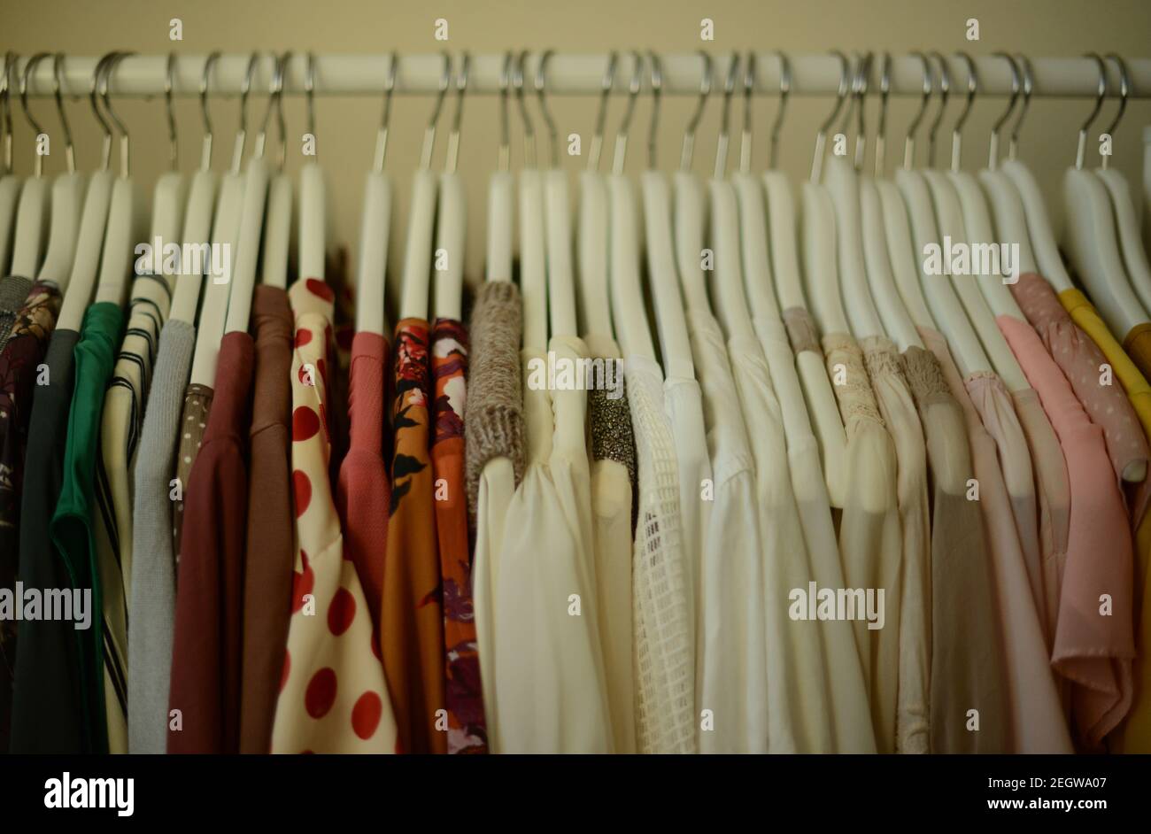blouses in different colors hanging on white hangers on a clothing rack in a row, arranged by color Stock Photo