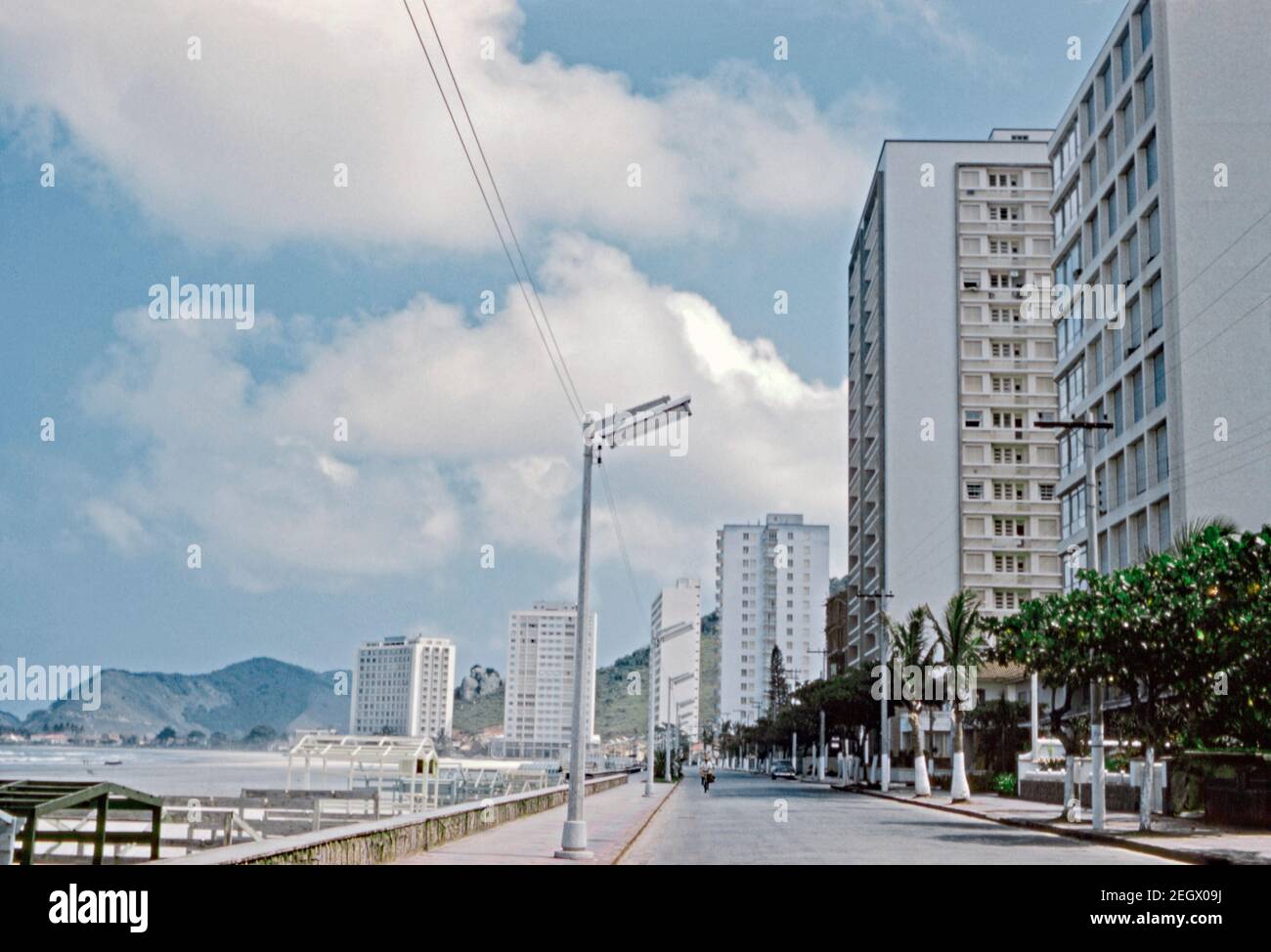 Looking west along the Avenida Marechal Deodora da Fonseca at Guarujá, São Paulo, Brazil 1961. High-rise apartment blocks start to dominate the beach-front scene even in the early 1960s. Guarujá is located in Santo Amaro island and is a city in the São Paulo state. This place name comes from the Tupi language, and means ‘narrow path’. This image is from an old amateur 35mm colour transparency. Stock Photo