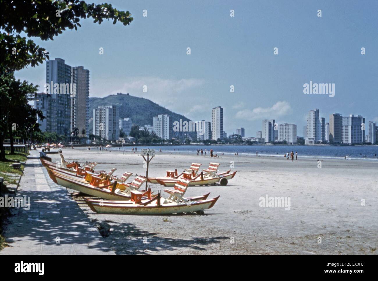 The beach front at Santos, Brazil 1961. High-rise apartment blocks dominate the beach-front scene even in the early 1960s. Rowing boats (barcos) are available for hire. Santos is a city in the Brazilian state of São Paulo, founded in 1546 by the Portuguese nobleman Brás Cubas. It is located mostly on the island of São Vicente, which is home to both the city of Santos and the city of São Vicente, and partially on the mainland. This image is from an old amateur 35mm colour transparency. Stock Photo