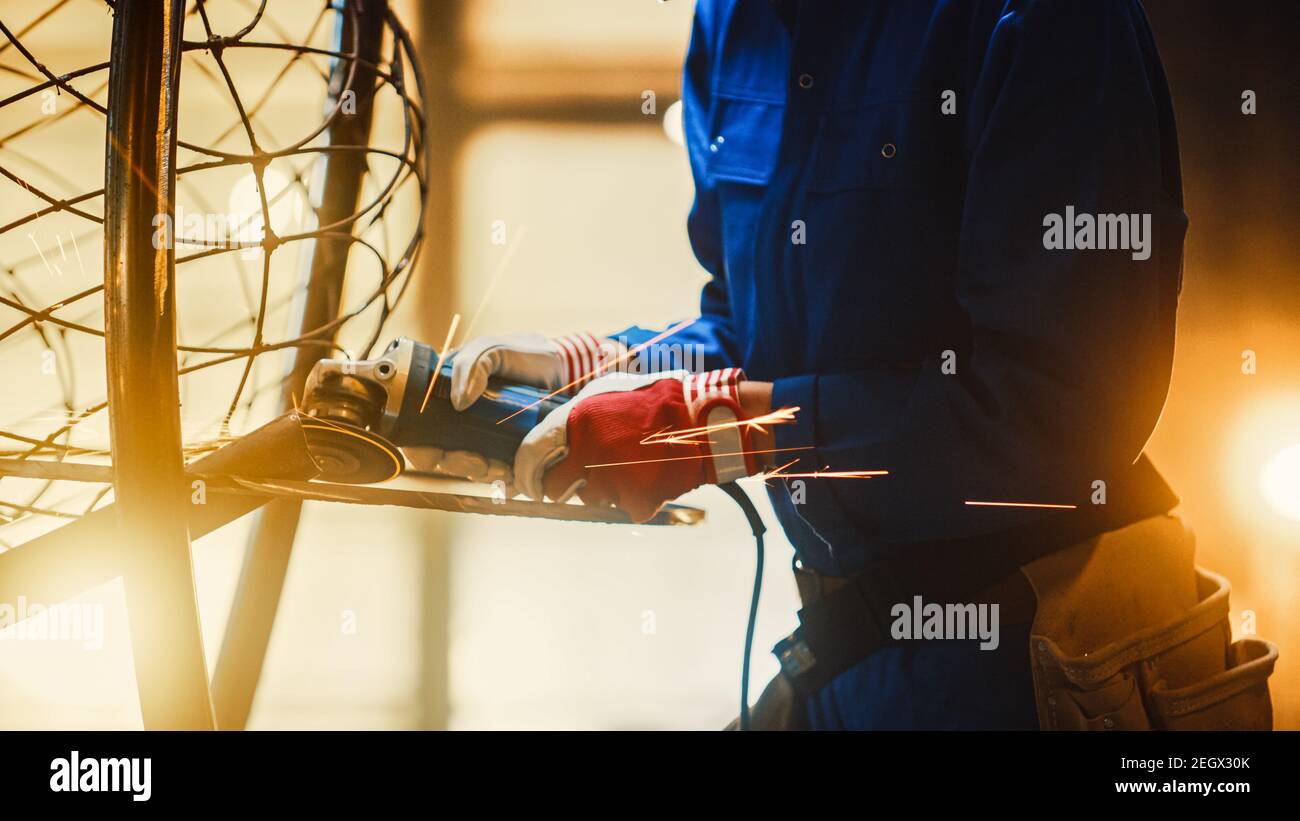 Close Up of Young Female Fabricator in Blue Jumpsuit. She is Grinding a Metal Tube Sculpture with an Angle Grinder in a Studio Workshop. Empowering Stock Photo