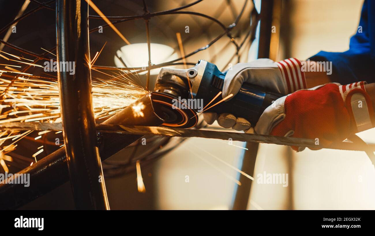 Close Up of Hands of a Metal Fabricator Wearing Safety Gloves and Grinding a Steel Tube Sculpture with an Angle Grinder in a Studio. Working with a Stock Photo