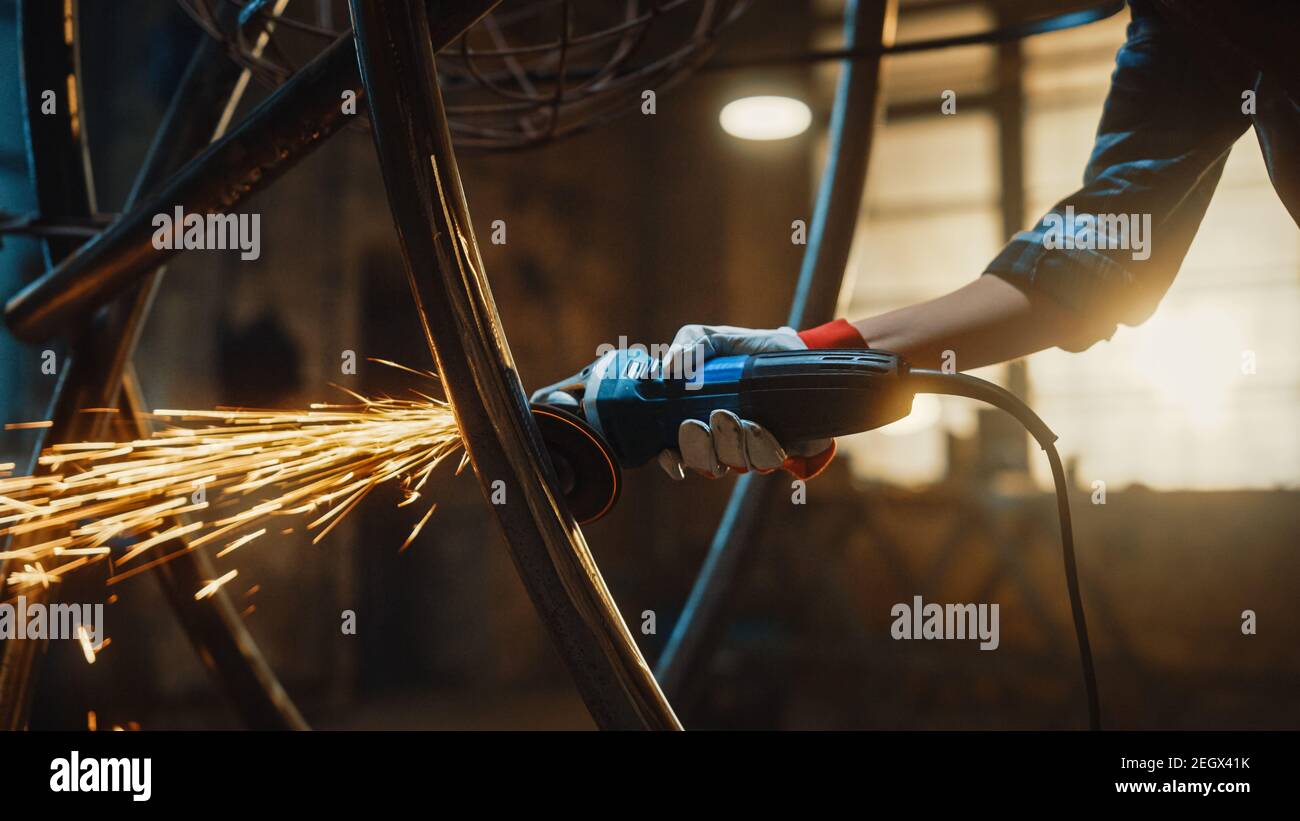 Close Up of Hands of a Metal Fabricator Wearing Safety Gloves and Grinding a Steel Tube Sculpture with an Angle Grinder in a Studio. Working with a Stock Photo