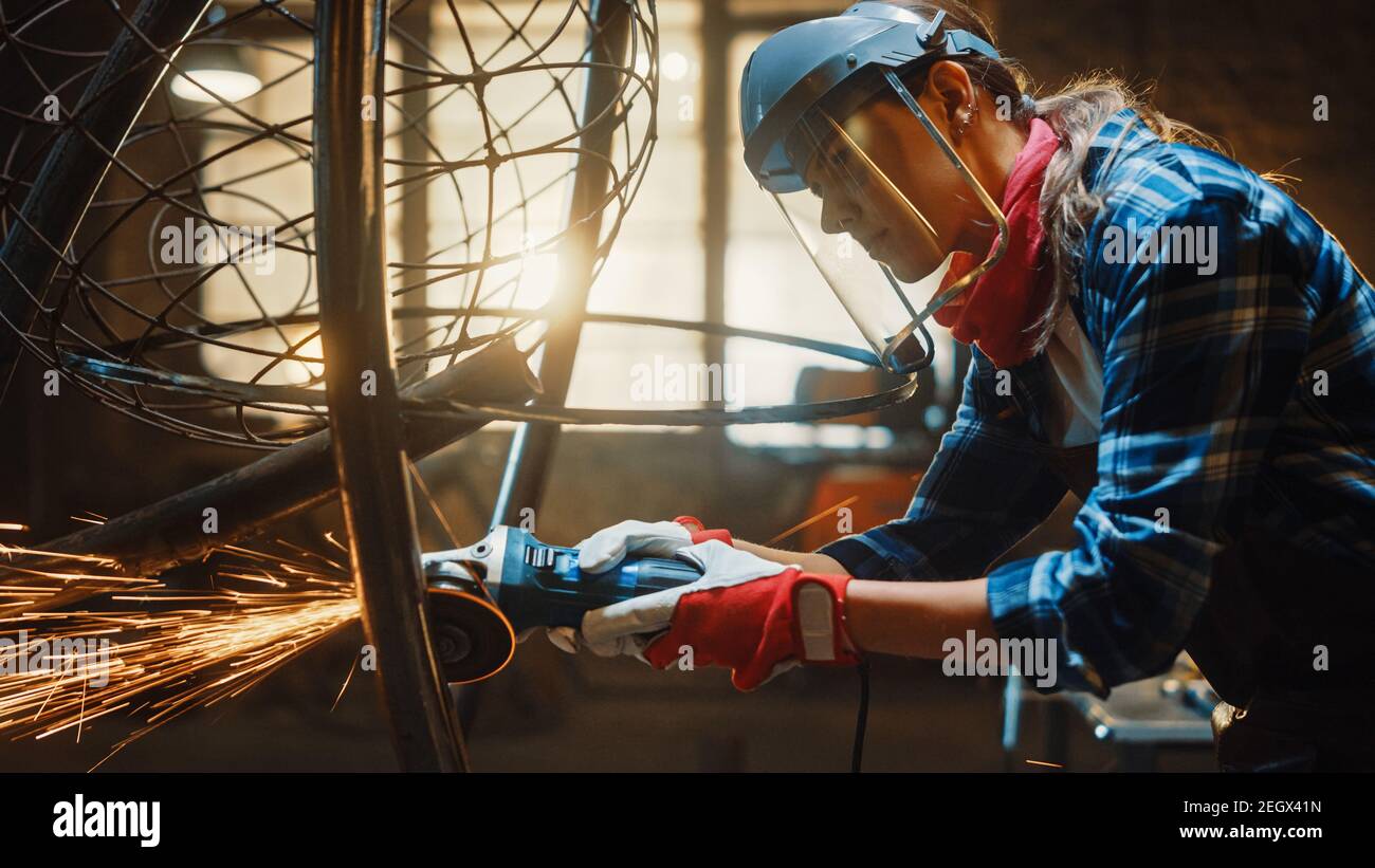 Close Up of Young Female Fabricator in Safety Mask. She is Grinding a Metal Tube Sculpture with an Angle Grinder in a Studio Workshop. Empowering Stock Photo