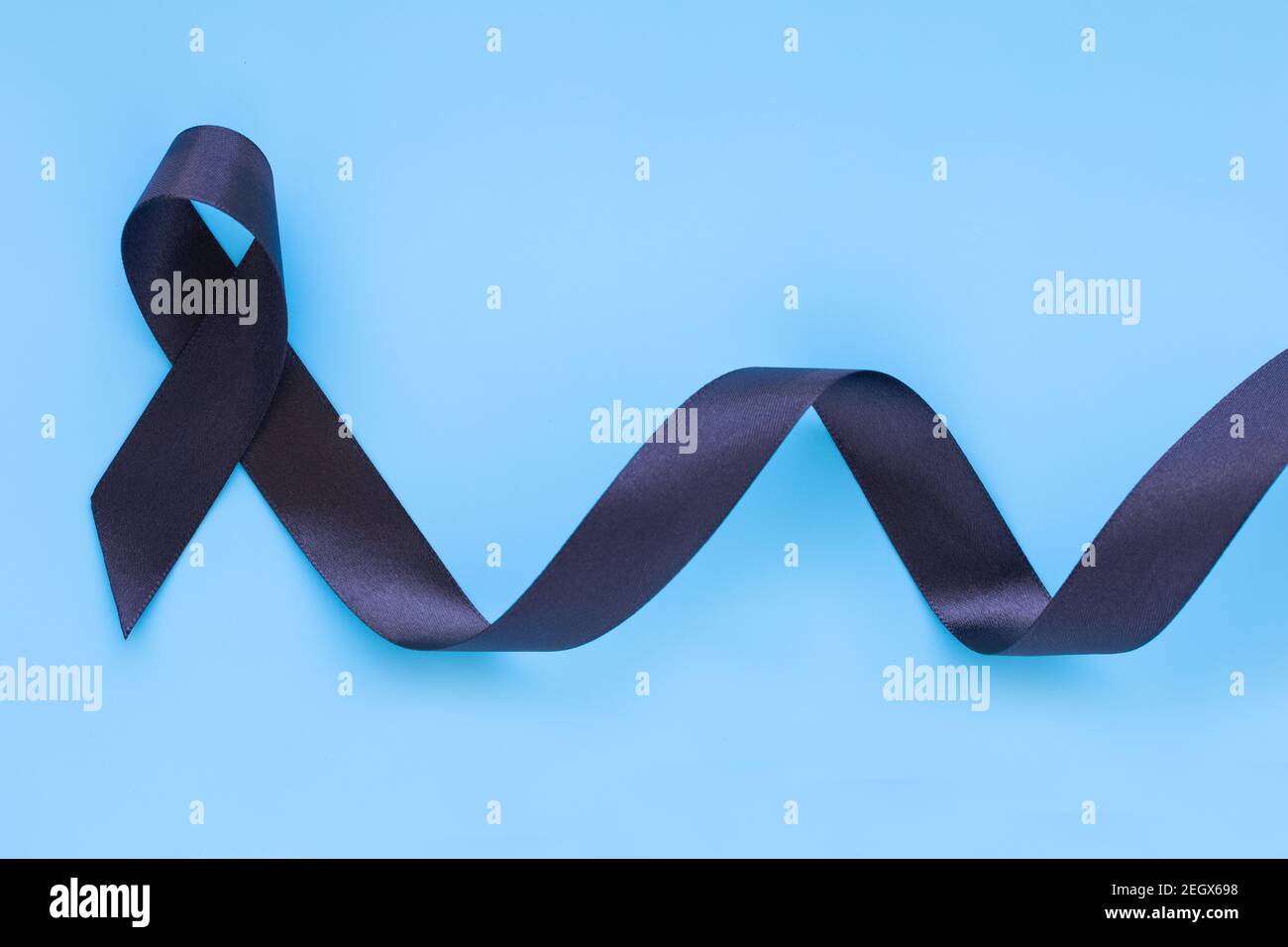 Black ribbon curl on blue isolated background with copy space, symbol of Skin Cancer awareness month on May, Melanoma cancer, Mourning ribbon symbolic Stock Photo