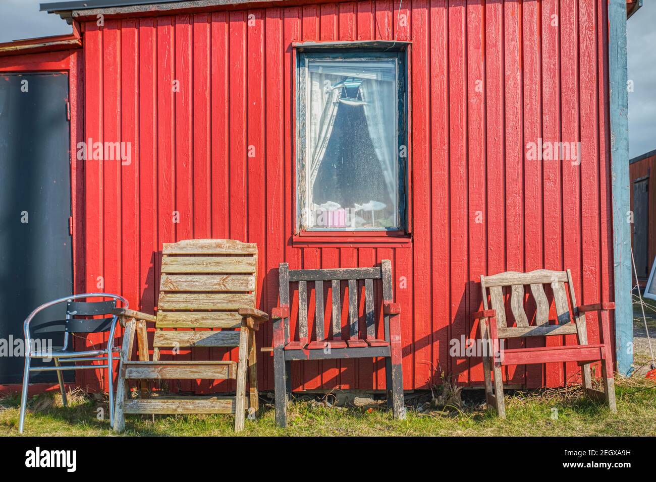 Traditional Scandinavian summerhouse facade with rectangular window and old chairs against the red wooden exterior made of planks and fish decoration Stock Photo