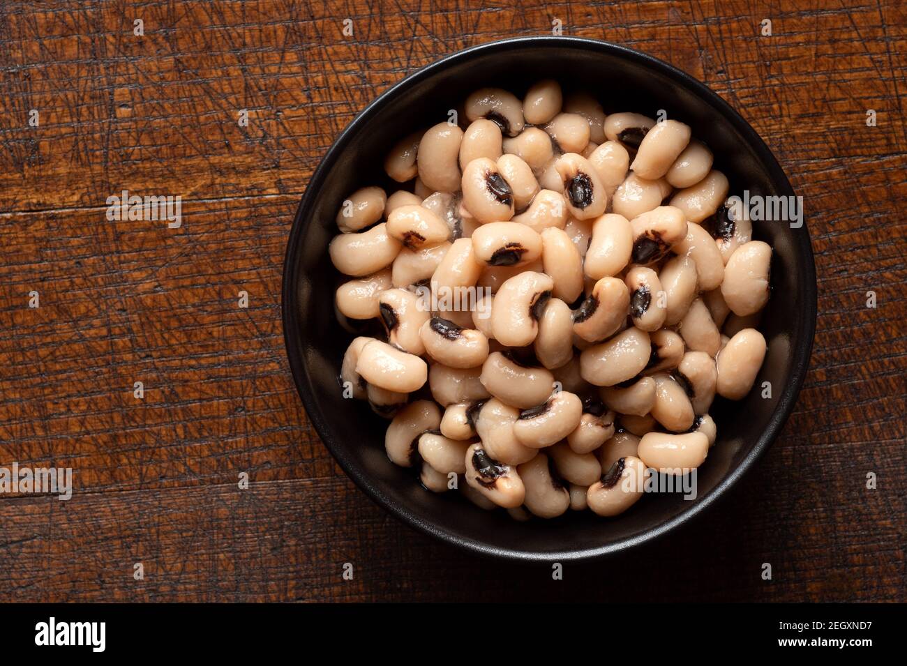Cooked black-eyed beans in a black ceramic bowl isolated on wood. Top view. Stock Photo