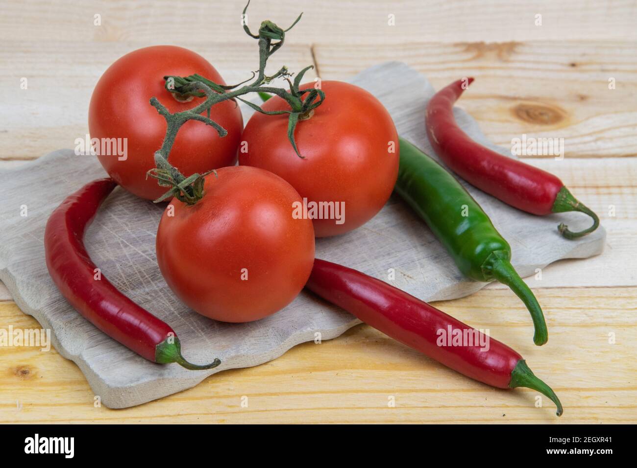 3 tomatoes and 4 hot peppers on a wooden board. Stock Photo