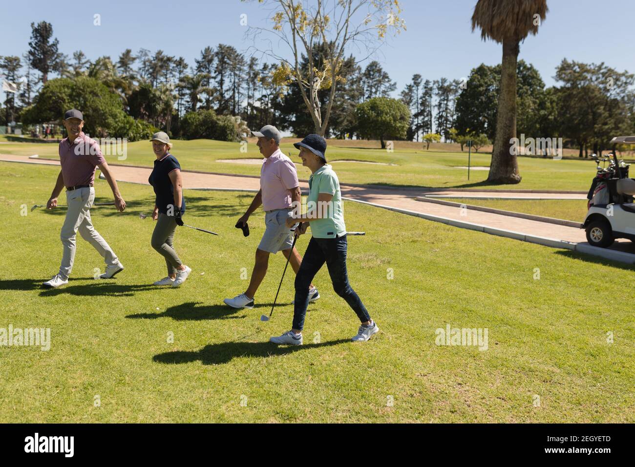 Four caucasian senior men and women walking away from baggies holding golf clubs Stock Photo