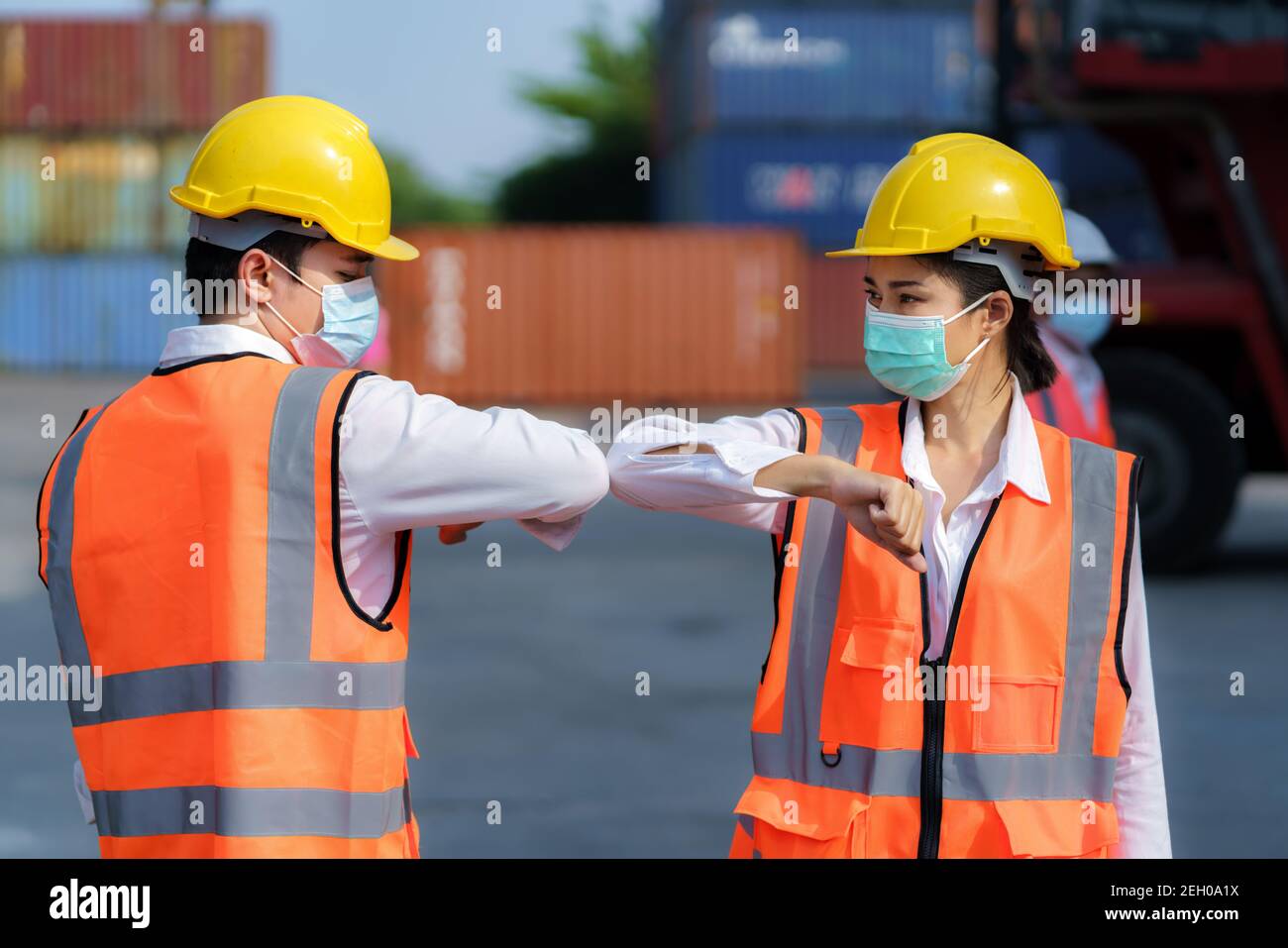 Asian worker new normal greeting by elbows bump wear safety helmet and mask in container depot terminal for prevent coronavirus and social distancing Stock Photo