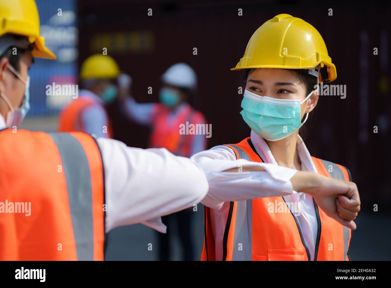 Asian worker new normal greeting by elbows bump wear safety helmet and mask in container depot terminal for prevent coronavirus and social distancing Stock Photo