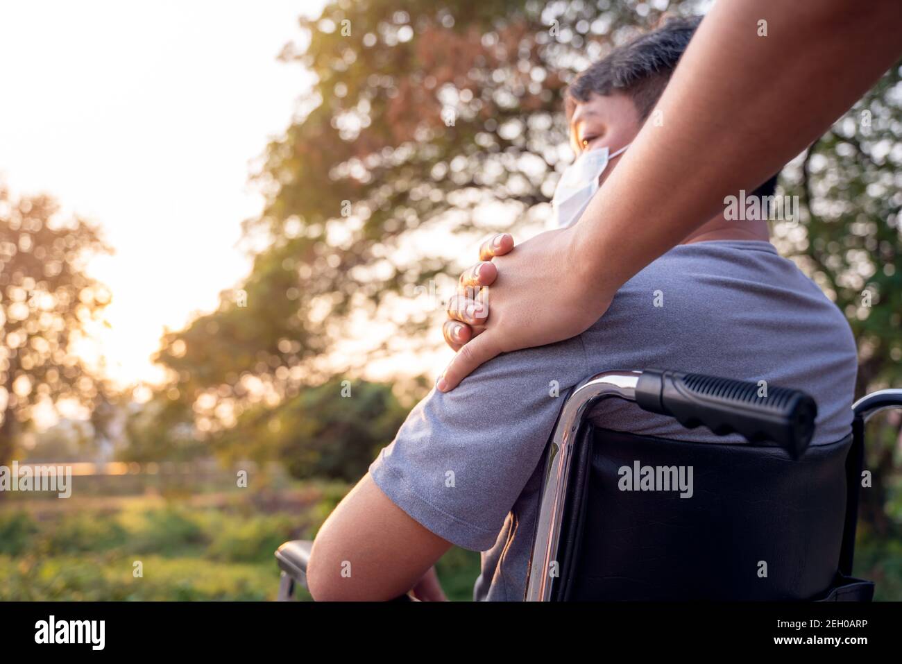 Close up hand patient or disabled man is sitting in wheelchair and young son on a walk in spring nature. Stock Photo