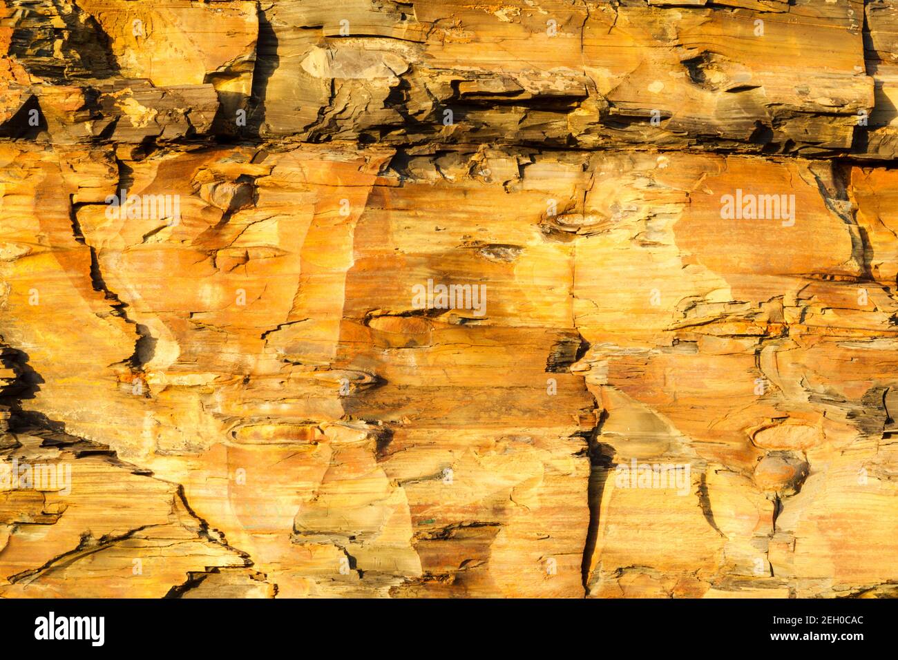Eroded cliff face made of sedementary deposits and occassional boulders in warm morning light showing rock layers and erosion process on north east co Stock Photo