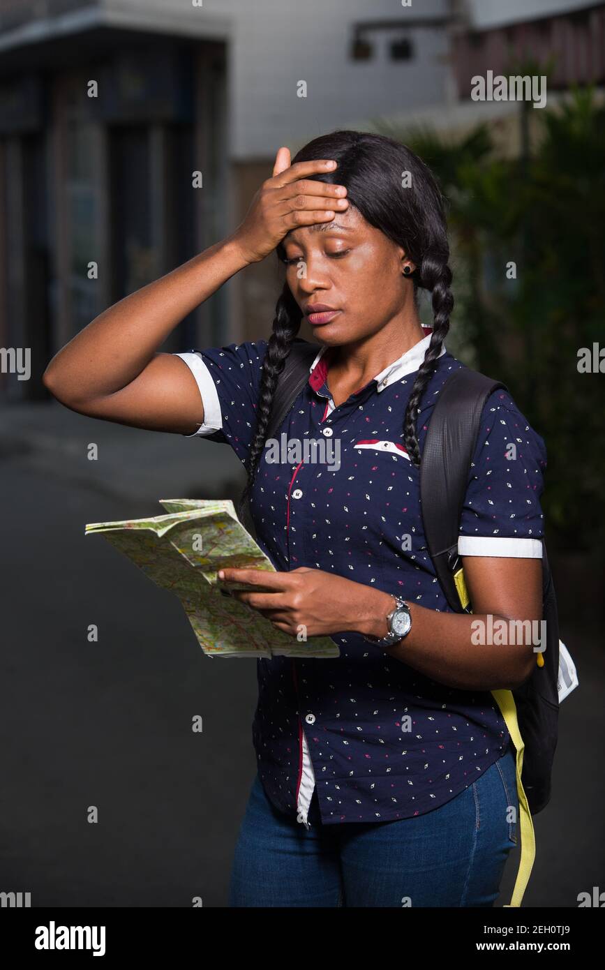 young female tourist standing in street backpack looking at map with hand on forehead. Stock Photo