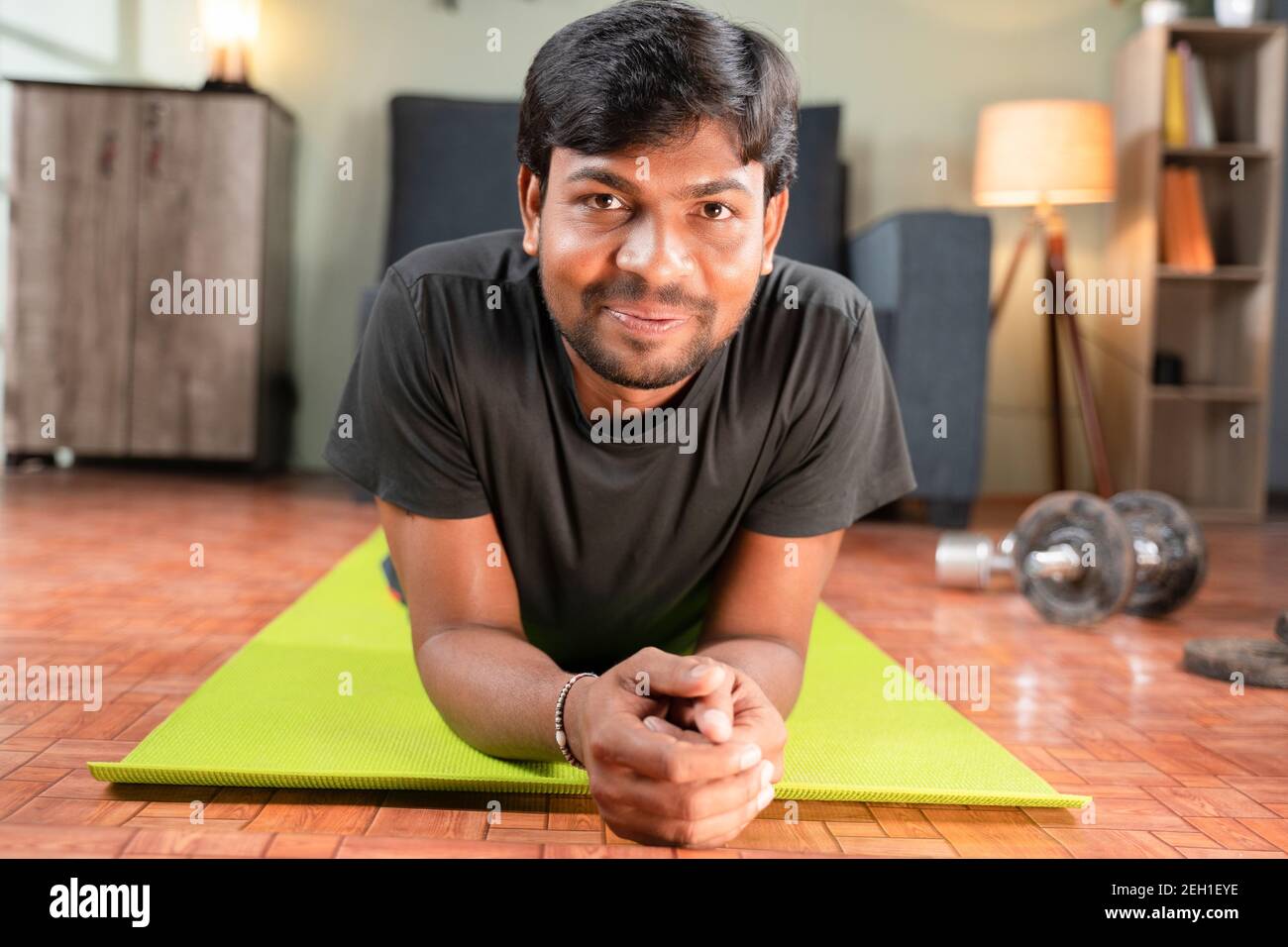 Young man with smiling face on yoga mat at home after working out looking camera, concept of home gym, new normal lifetyle, health and fitness. Stock Photo