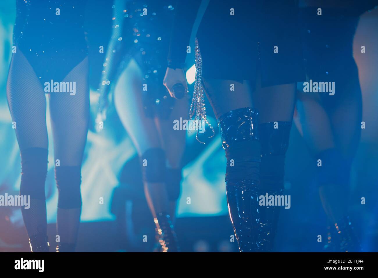 unrecognizable female pop group performing on stage four women in boots black pantyhose holding a microphone blue light. Stock Photo