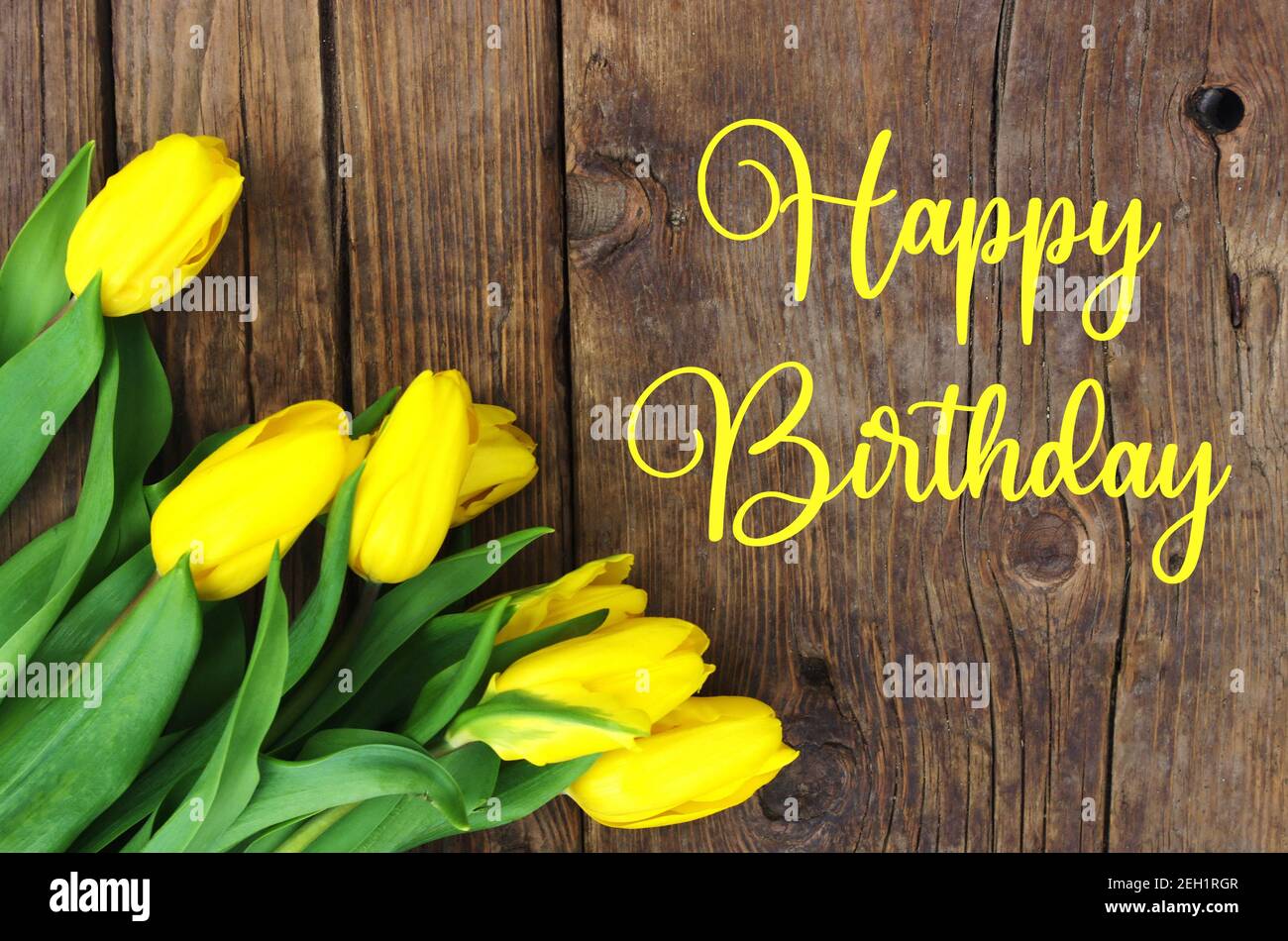 Happy Birthday text with Fresh yellow tulips on wooden vintage rustic bacground. Tulips on wooden board with text Happy Birthday. Greeting card. Stock Photo