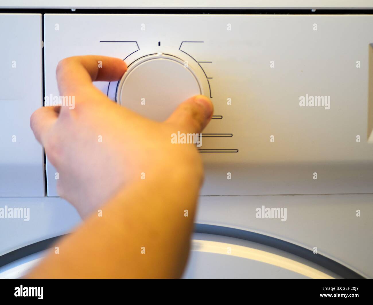 Mode selector for washing machine, tumble dryer. Without words. Hand selecting a mode. White washing machine. Concept, modern. Horizontal view. Stock Photo
