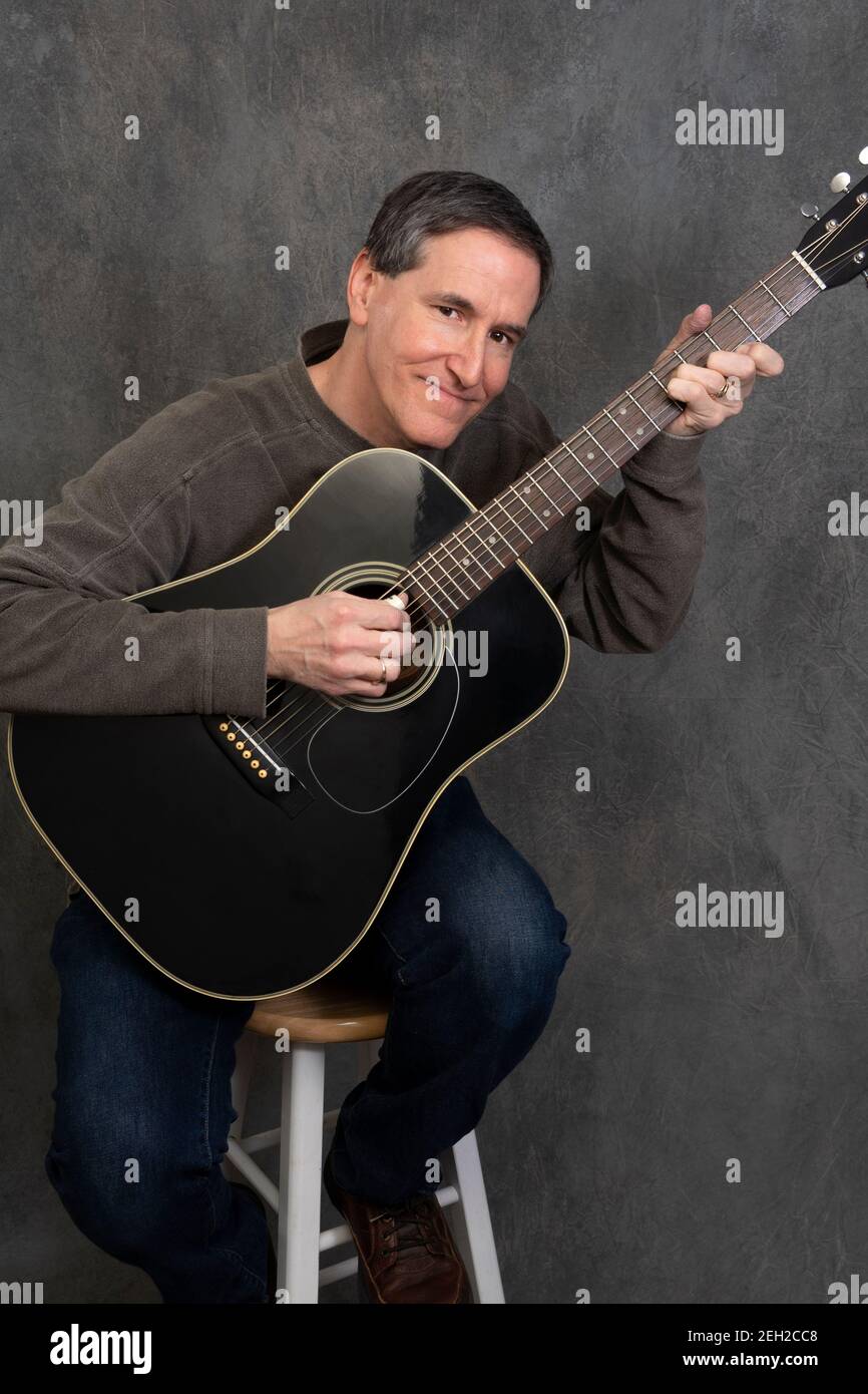 man sitting on stool playing acoustic steel stringed guitar Stock Photo