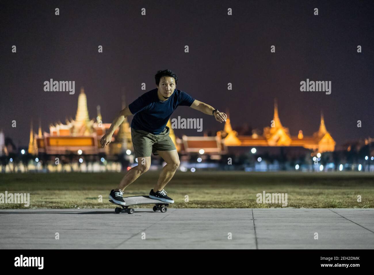 Asian Cheerful man playing surfskate or skate board in outdoor Park at  night over photo blur of Bangkok Grand Palace,Thailand, low light, extream  spor Stock Photo - Alamy