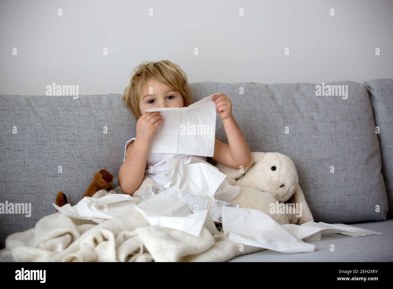 Blond toddler child, wiping his nose in a tissue, sneezing and coughing