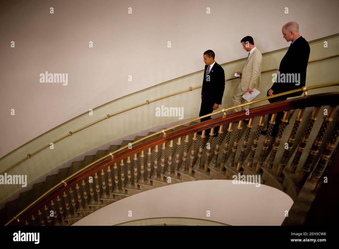 President Barack Obama walks down a spiral staircase with aide Brian Mosteller and a U.S. Secret Service agent after taping his weekly address in the Eisenhower Executive Office Building on July 24, 2009. Stock Photo