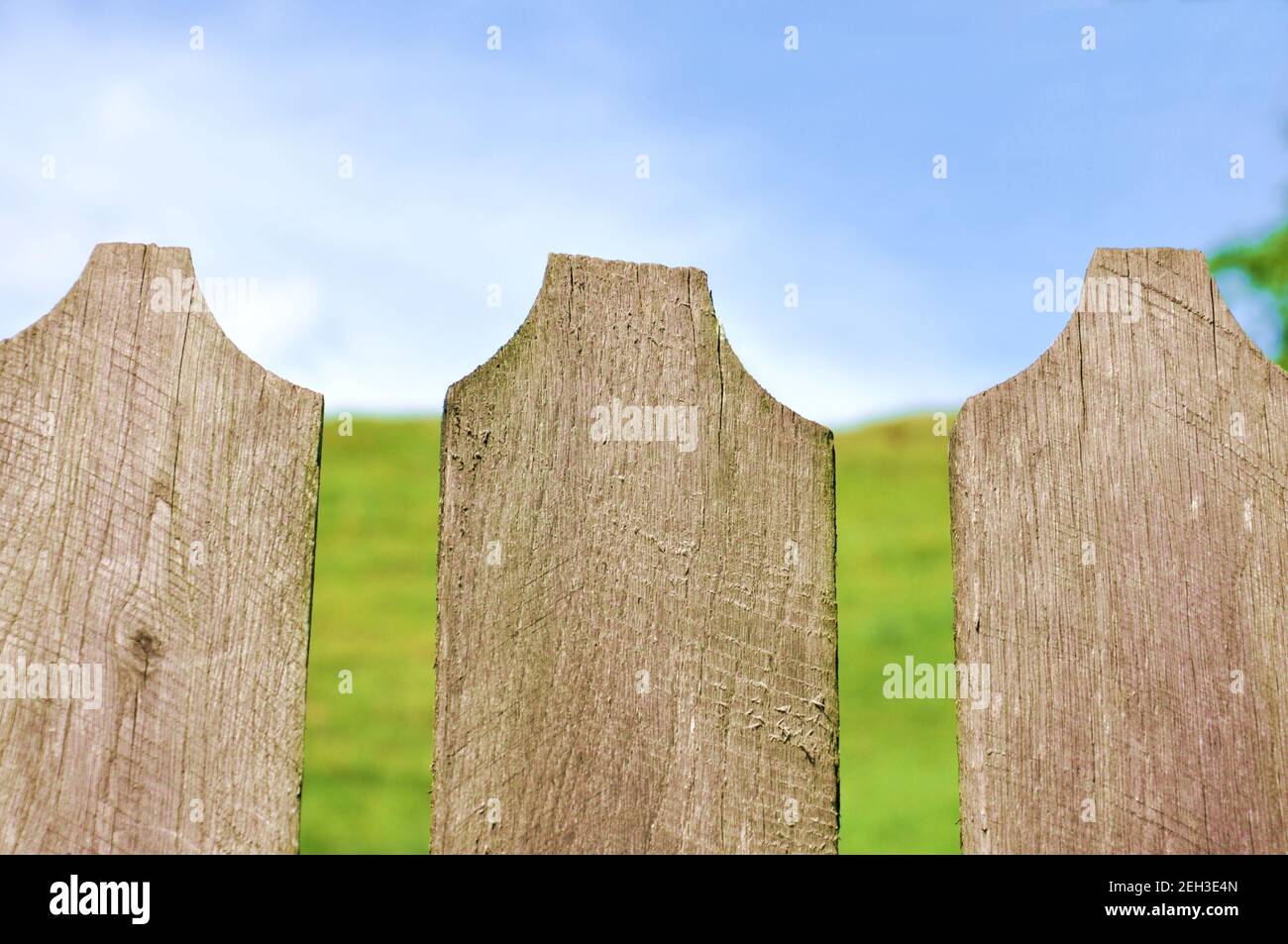 Three wood gray fences in the foreground with green meadows in background and the blue sky, close up, selective focus, copy space, saturated tone Stock Photo