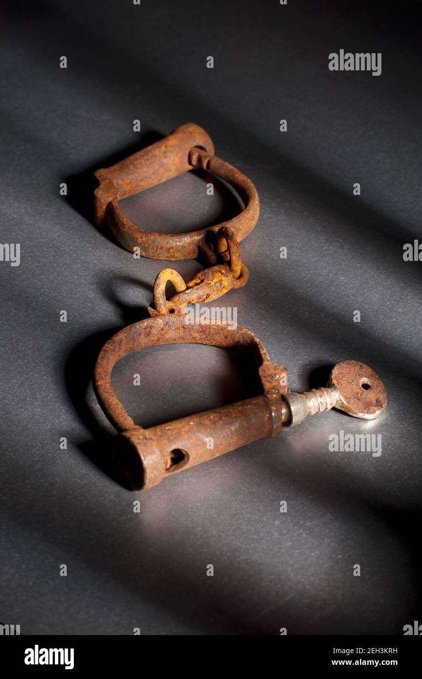 Vintage hand-cuffs on grey background with window bar shadows. Stock Photo