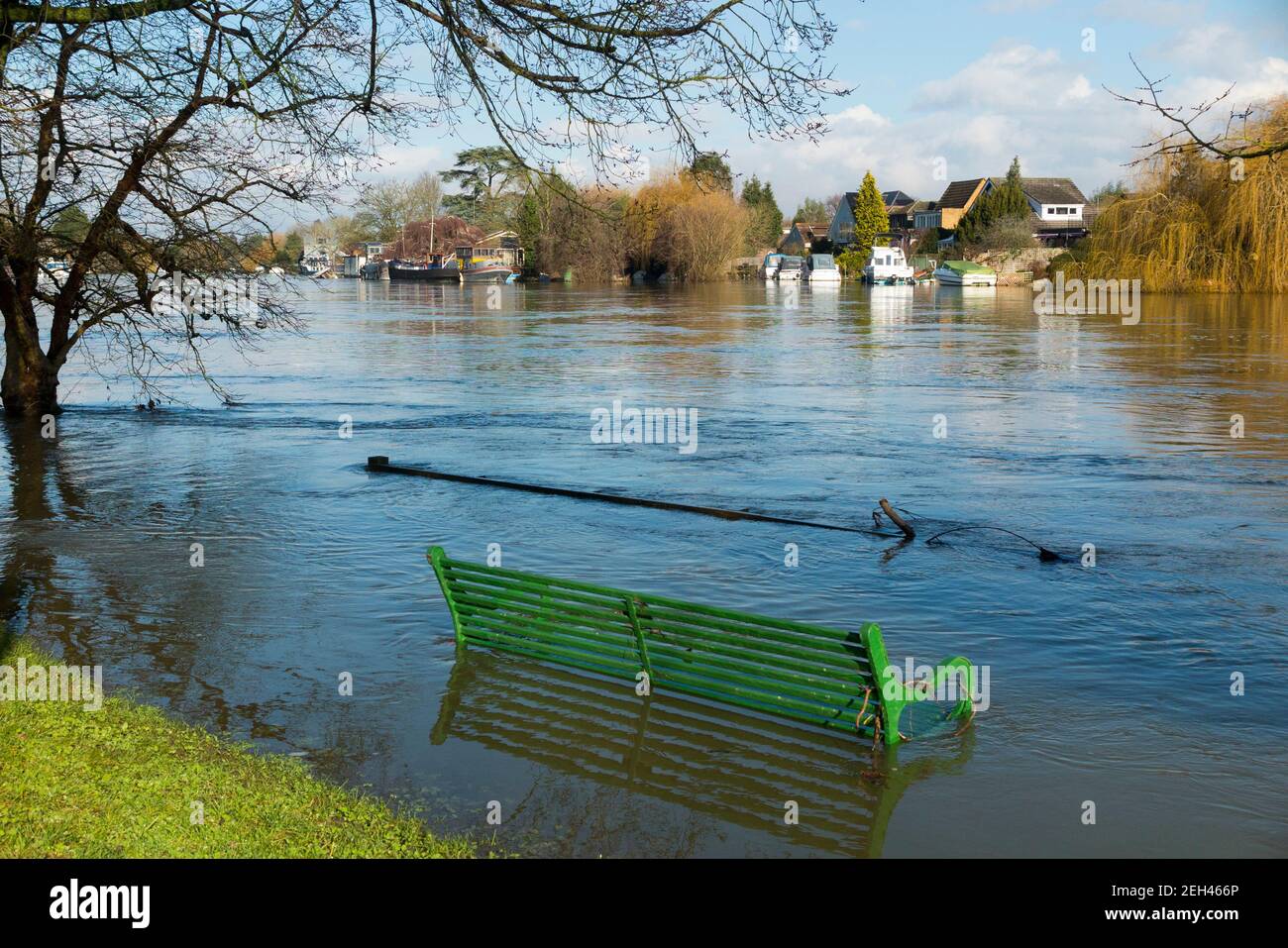 A partially submerged park bench seat in flood waters of the river Thames in old Windsor near Runnymede meadows & flood plain, site of the the signing of the Magna Carta in the year 1215 by King John and the English barons. Winter day with sunny sun and blue sky skies. (123) Stock Photo