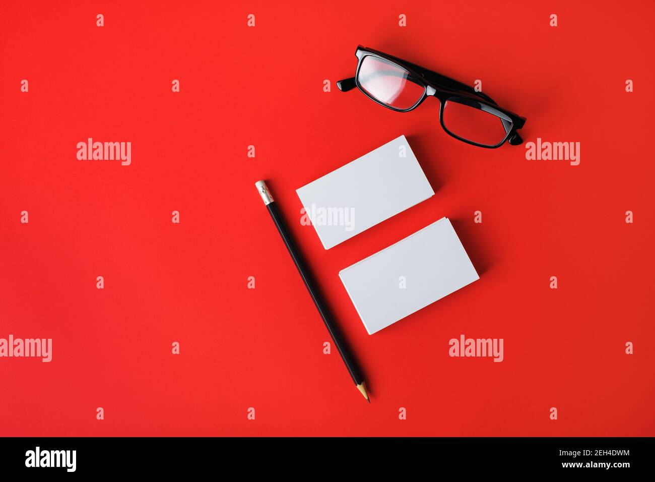 Blank business cards, pencil and glasses on red background. Mock-up for branding identity. Top view. Flat lay. Stock Photo