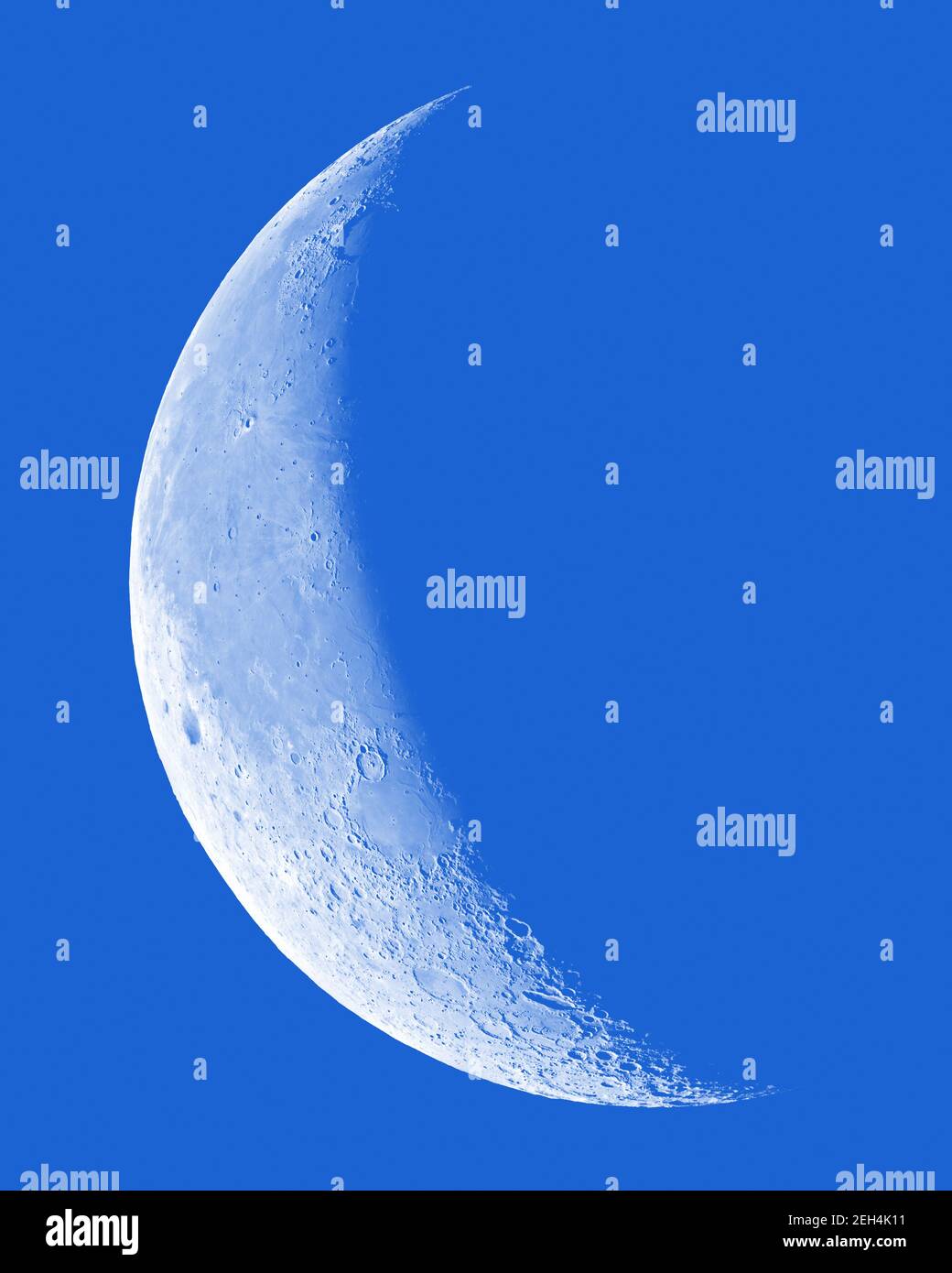 Waning Crescent Moon with crater detail on blue sky. Stock Photo