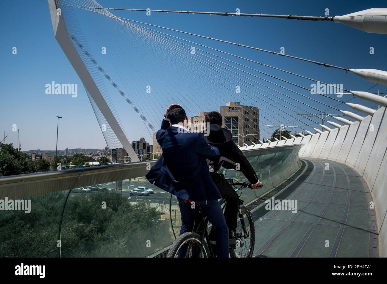 Two Jews ride their bikes over the Cordes Bridge. This one is now part of the Jerusalemite landscape. With its steel cables connecting the structure to a sort of mast, the futuristic work of Spanish architect Santiago Calatrava allows the tramway to cross a busy intersection in Jerusalem, on the road leading to Tel Aviv. A footbridge with glass railing adjacent to the tramway has been provided for pedestrians. May 17, 2018. Jerusalem. Israel. Stock Photo