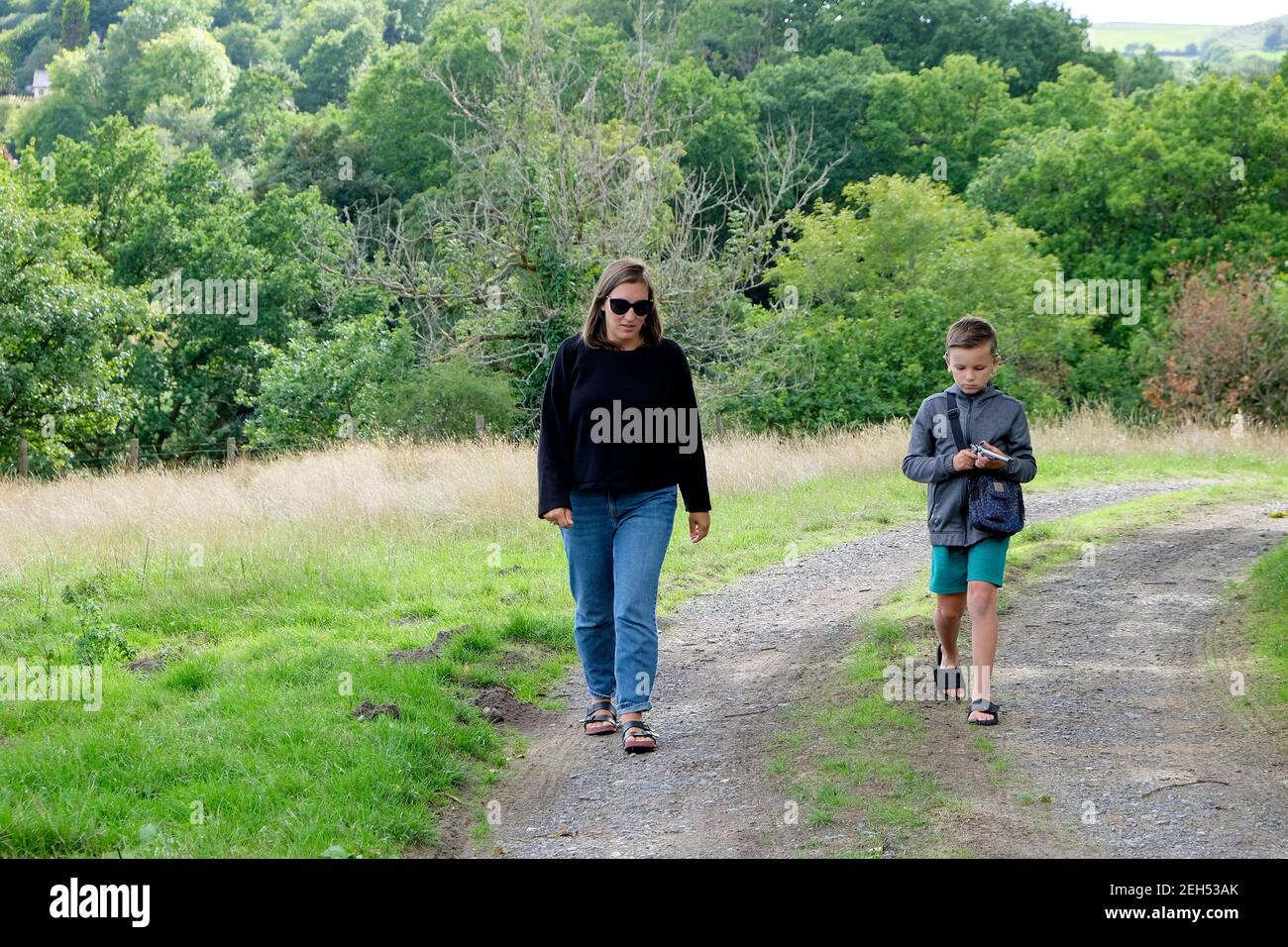 Mother and son walk walking along a country track on road lane path in rural Welsh summer countryside trees Carmarthenshire Wales UK KATHY DEWITT Stock Photo