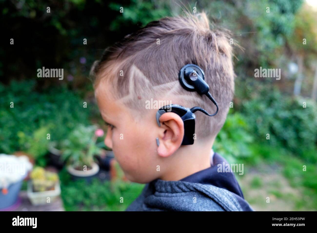 Cool star shape hairstyle on deaf boy child 8 with cochlear implant implants side view profile outside in garden Wales UK Britain   KATHY DEWITT Stock Photo