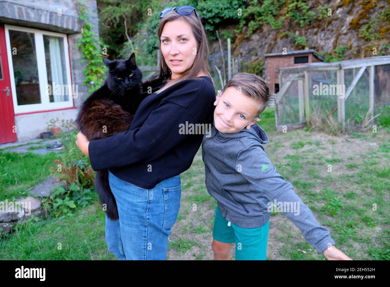 Woman holding black cat mother and boy son child looking at camera posing having fun making silly facial expressions outside in garden UK KATHY DEWITT Stock Photo