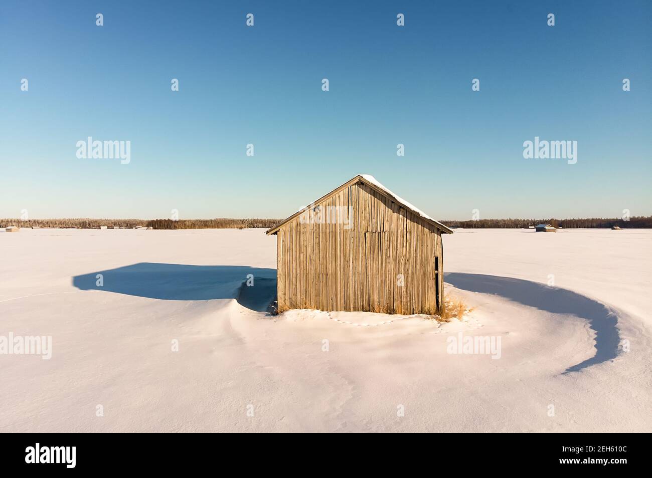 The winter sun creates strong shadows on the snowy fields. The old barn house stands alone on the vast fields. Stock Photo