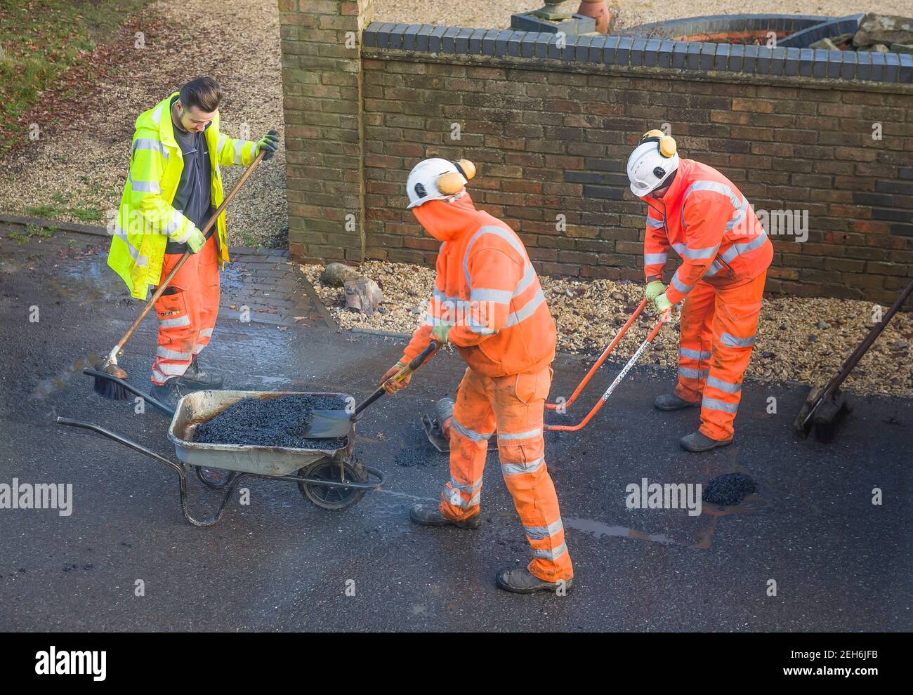 BUCKINGHAM, UK - December 14, 2020. Road workers wearing high visibility hi vis orange clothing, repairing potholes in a street Stock Photo