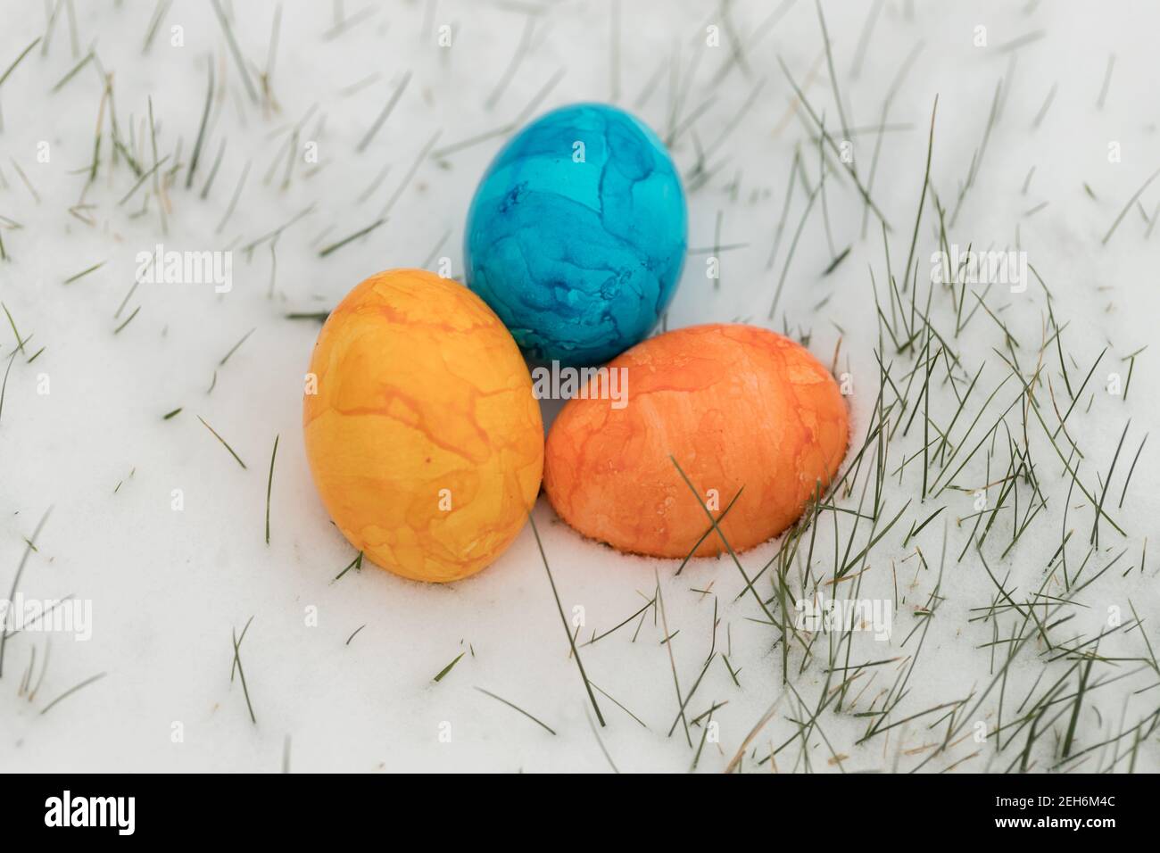 close-up of three colorful easter eggs in the snow with little blade of grass Stock Photo