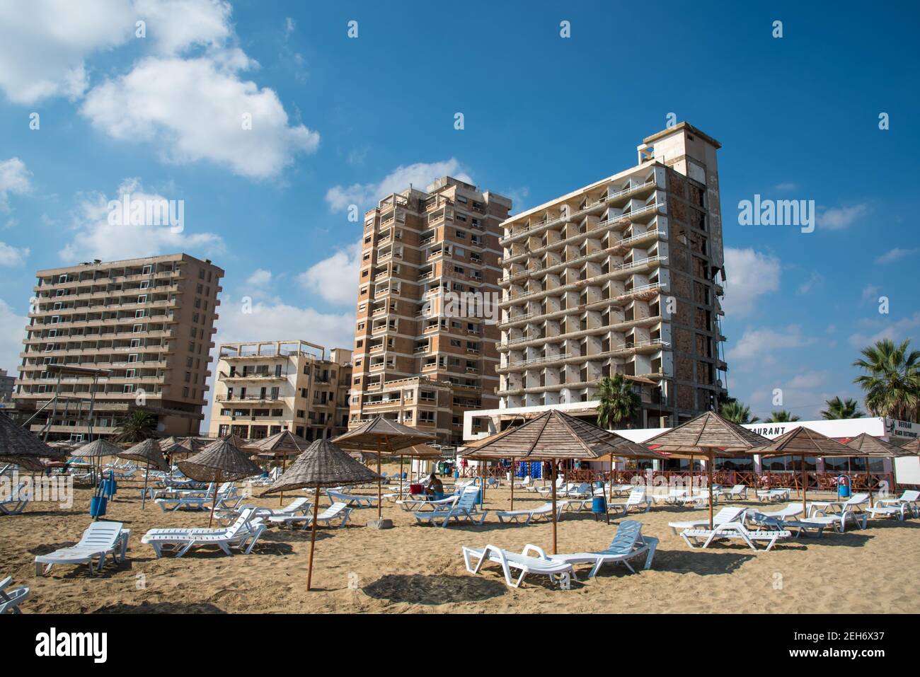 Palm Beach with beach umbrellas and tourists and abandoned hotels at ghost town, Famagusta, Northern Cyprus Stock Photo