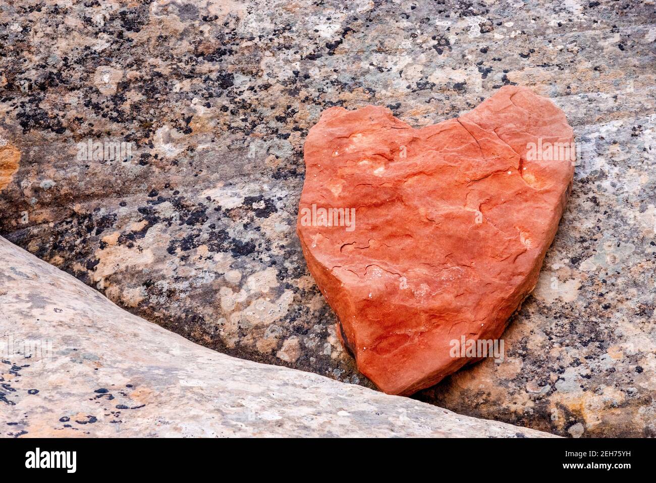 Red heart shape rock laying on granite rock. Valentine card appropriate. Stock Photo
