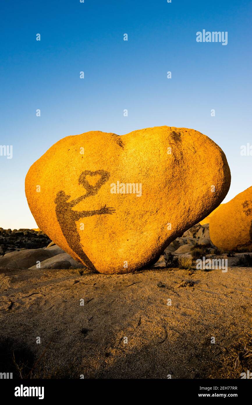 Heart shaped boulder with shadow of man holding a heart wreath. In golden evening light at Joshua Tree National Park, CA Valentine card appropriate. Stock Photo