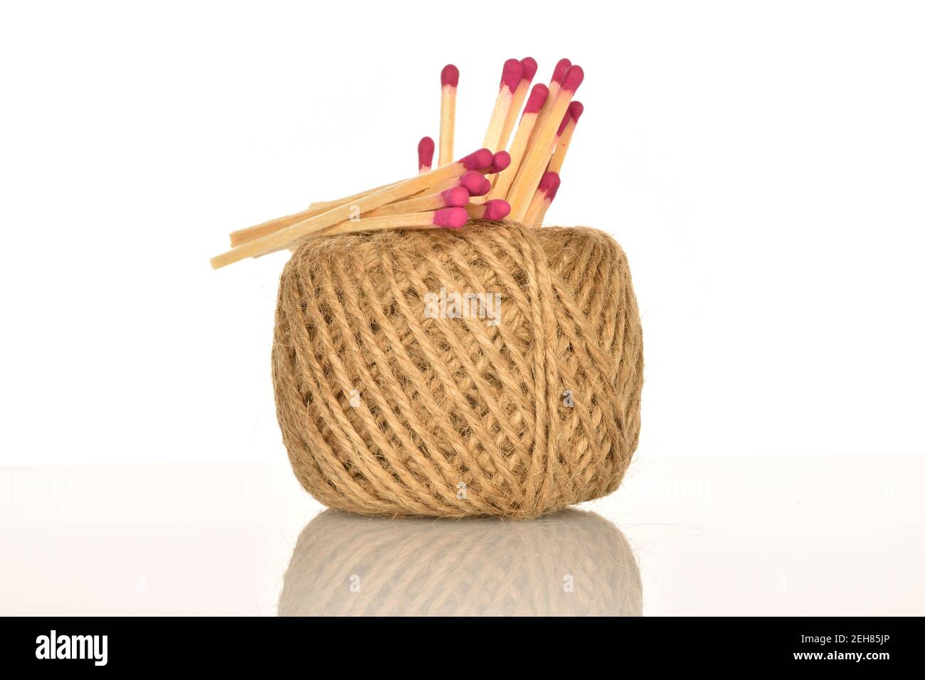 Several wooden matches with a ball of jute thread on a white background