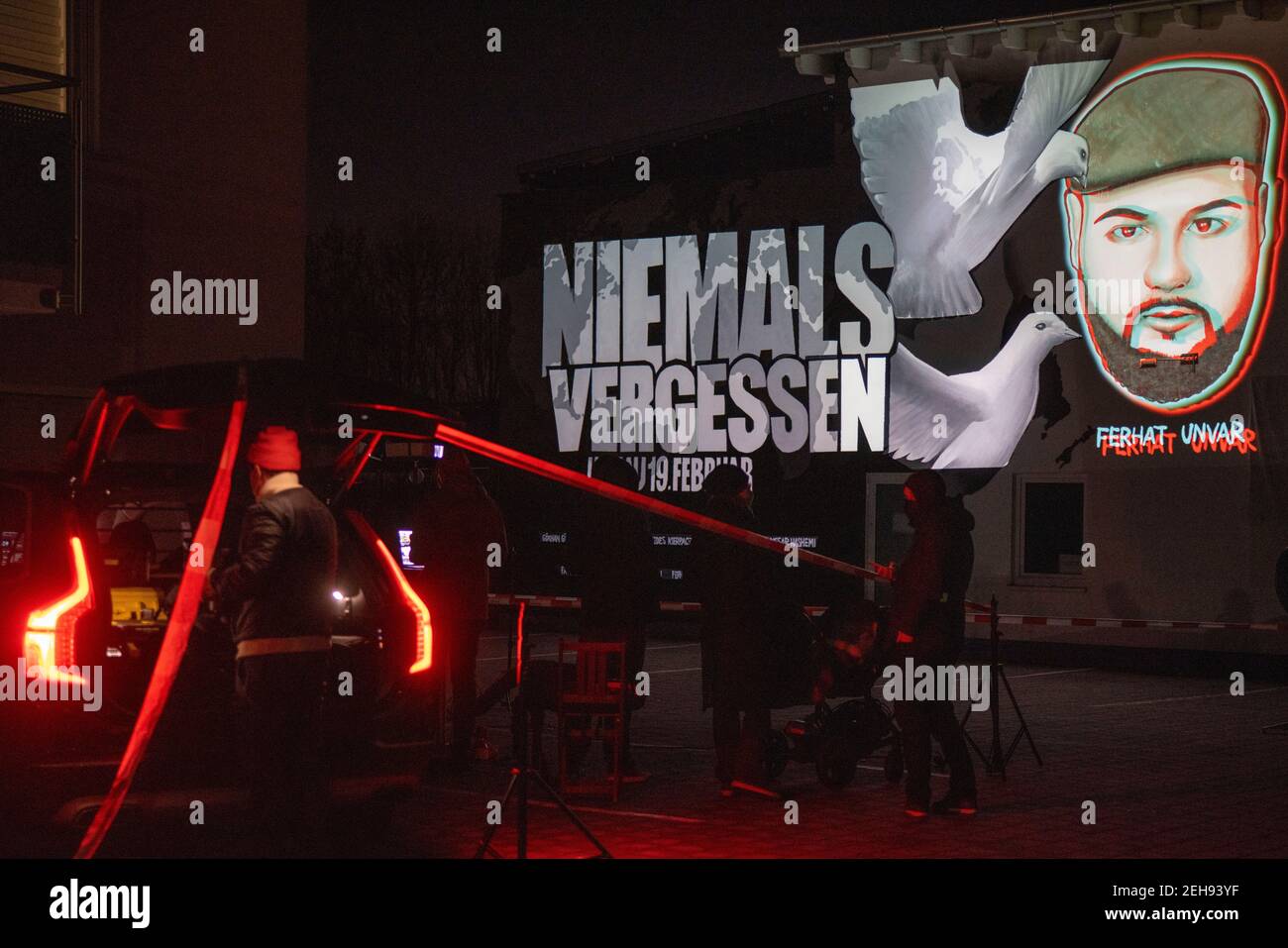 19 February 2021, Hessen, Bruchköbel: In front of a shisha bar in Bruchköbel near Hanau, a group of people gathered to commemorate the racist murder on the anniversary of the attack in Hanau. The faces of the murdered people were projected on the outside wall of the bar with graffiti and a light installation. A right-wing extremist had shot nine people in Hanau on 19 February 2020 for racist motives. Subsequently, the man had shot his mother and then himself. The act caused worldwide horror. Photo: Helmut Fricke/dpa Stock Photo