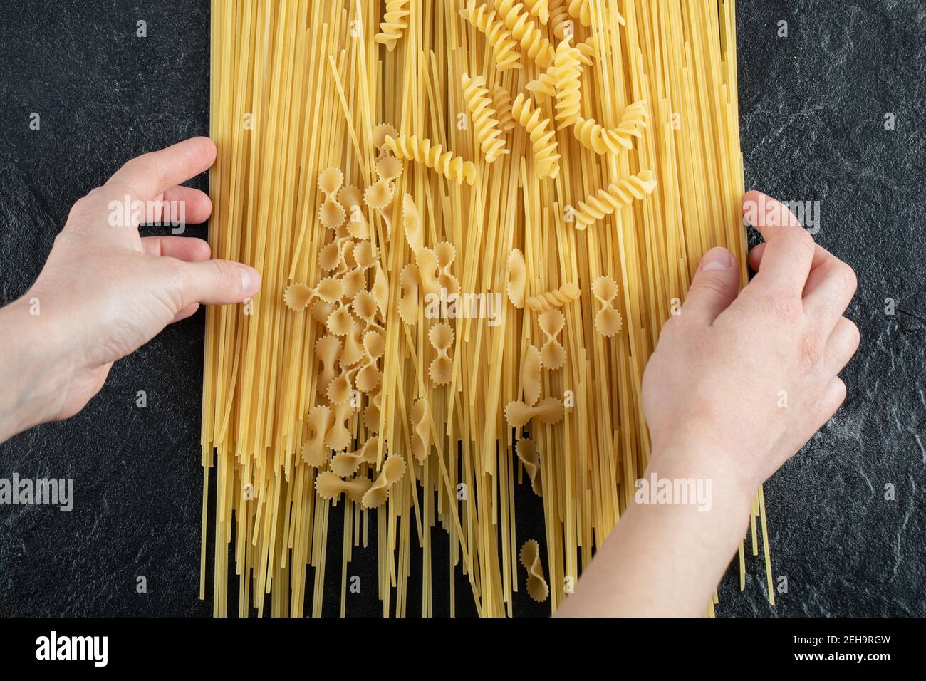 Woman hands touching various pasta on dark surface Stock Photo