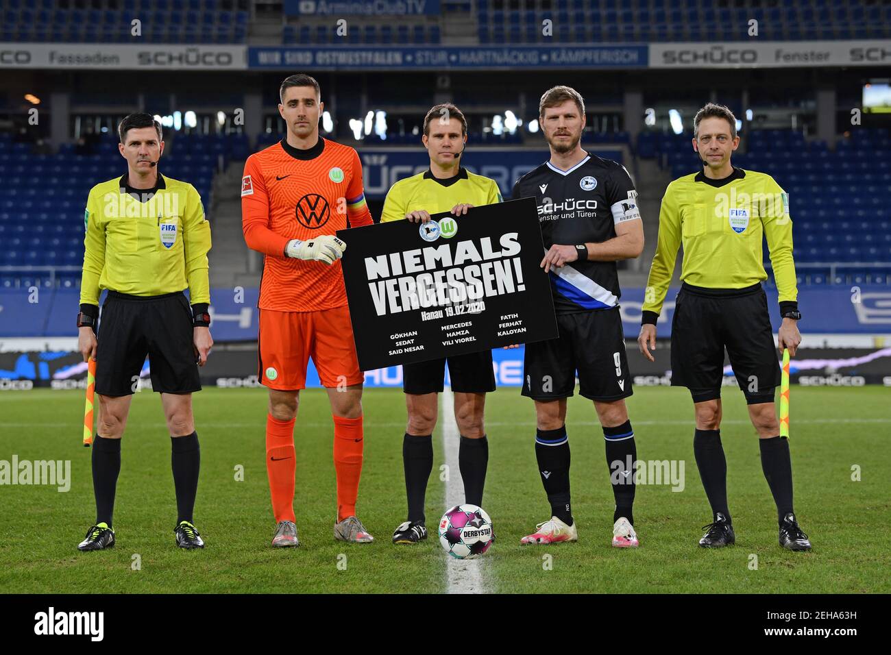 Bielefeld, Germany. 19th Feb, 2021. Football: Bundesliga, Arminia Bielefeld - VfL Wolfsburg, Matchday 22 at Schüco Arena. Stefan Lupp (l-r), assistant referee, Koen Casteels, team captain of VfL Wolfsburg, Felix Brych, referee, Fabian Klos, team captain of Arminia Bielefeld, and Mark Borsch, assistant referee, hold a banner commemorating the racist attack in Hanau a year ago. A right-wing extremist had shot nine people in Hanau on 19 February 2020 for racist motives. Subsequently, the man had shot his mother and then himself. The act caused worldwide horror. Credit: H/dpa/Alamy Live News Stock Photo