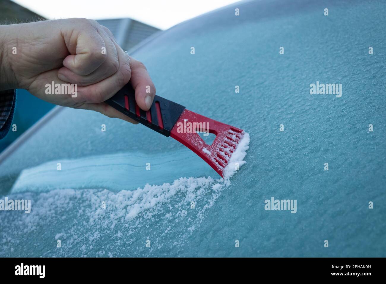 A man scraping ice off a frozen wind shield or screen of a vehicle on a cold winters morning Stock Photo
