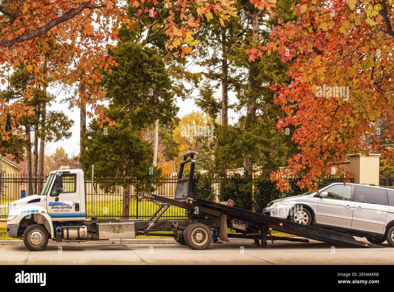 2018 11 18 Tulsa USA Tow truck with operator making adjustments a van is loaded on trailer on street on a beautiful and colorful autumn day in front o Stock Photo