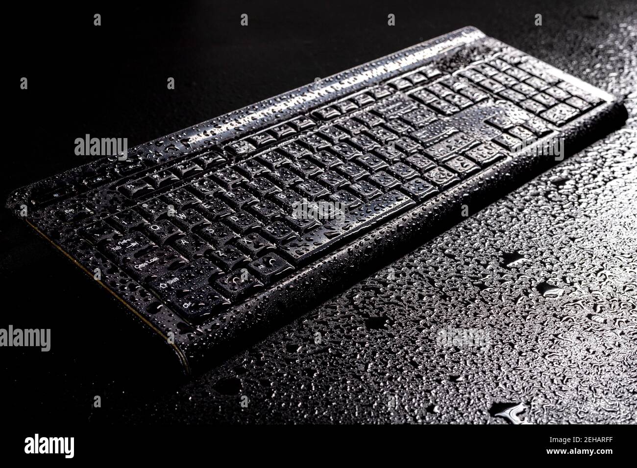Wet keyboard from a personal computer. Water drops on an electronic device. Dark background. Stock Photo