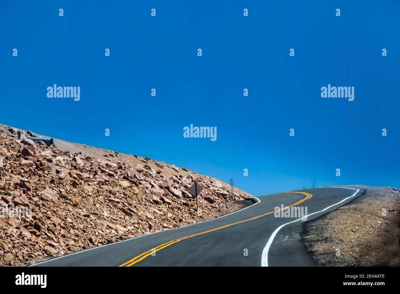 Driving mountain road into a hairpin curve with drop-off to one side and just the sky showing up above the tree line on Pikes Peak Colorado Stock Photo