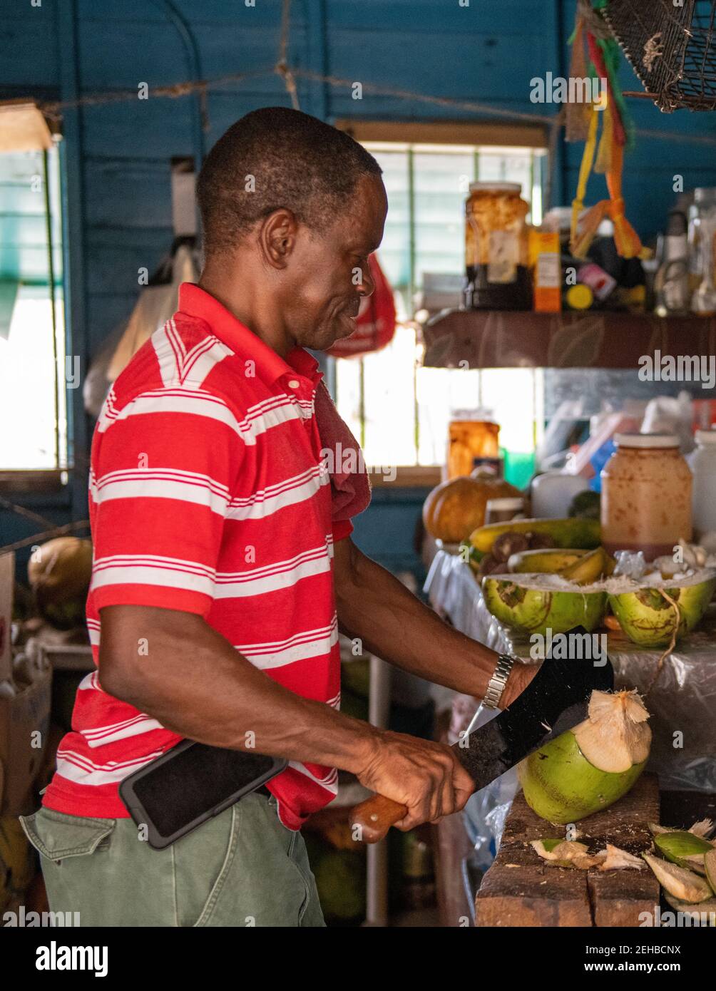 Afro-Caribbean man opening a coconut to sell to a tourist, Freeport, Bahamas, 2019 Stock Photo